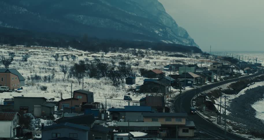 Snowy coastal village with a winding road by the sea and mountain