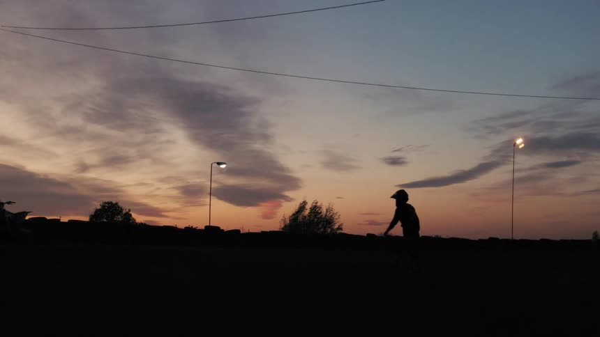 Silhouette of a person wearing a helmet walking outdoors in the late afternoon