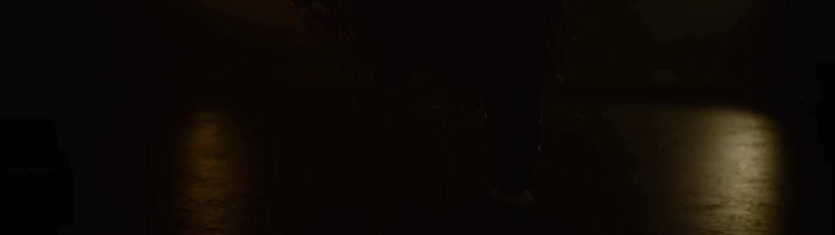 A dimly lit closeup shot focuses on the lower legs and feet of a person walking on a dark street at night