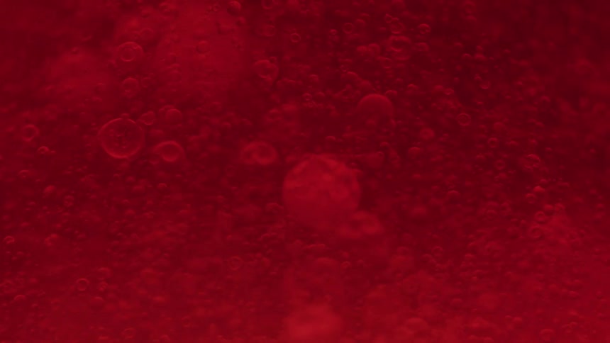 Red liquid with suspended bubbles in motion under a macro lens