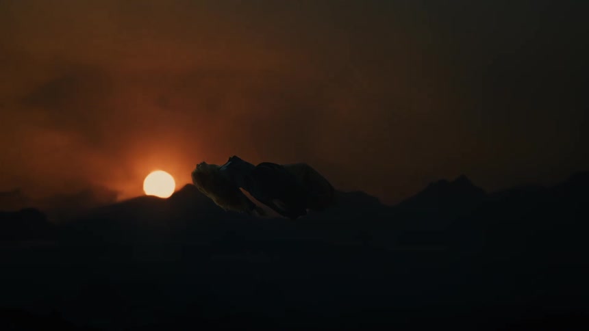 A bright orange sun sets behind a mountain range with a silhouetted woman ethereally floating under a dark cloudy sky