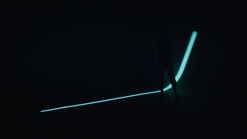 A person is walking in a dark room with a thin line of light passing over