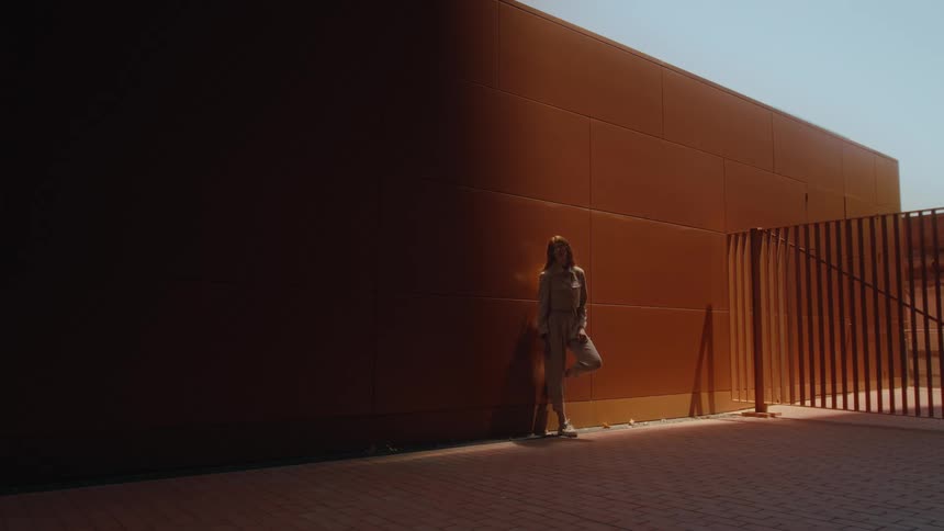 Woman leans against orange wall in partial sunlight