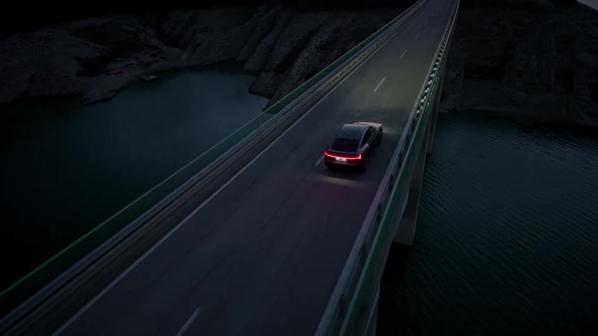 A sedan drives across a bridge with its headlights on illuminating the path in the dark