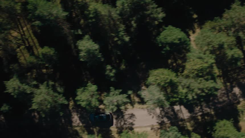 A car is driving along a winding forest road captured from above