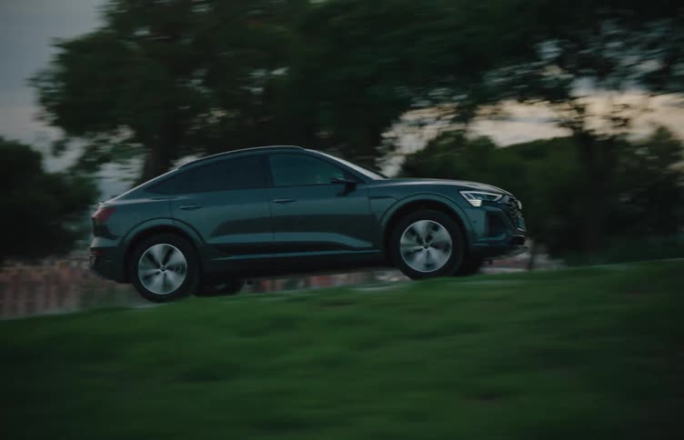 A sleek suv drives along a road with a city skyline and trees in the background