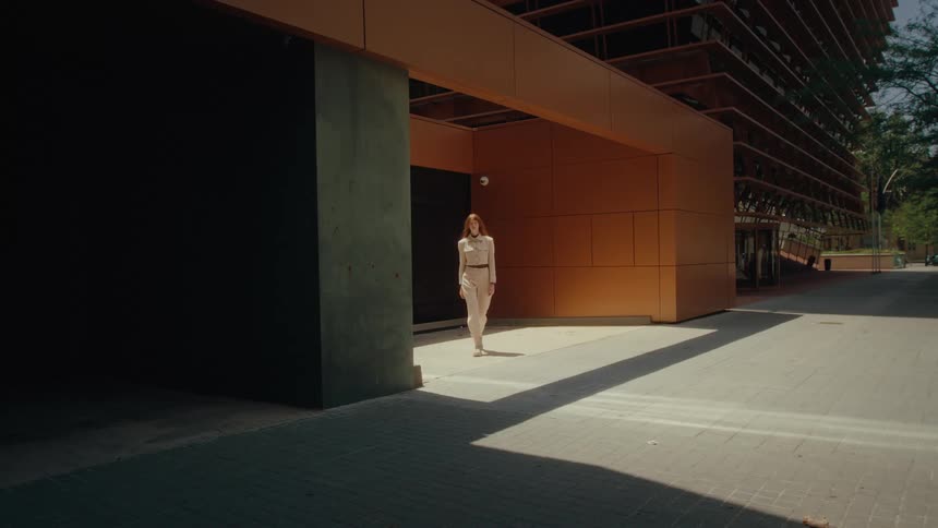A woman walks toward the camera through a modern shadowfilled architectural corridor