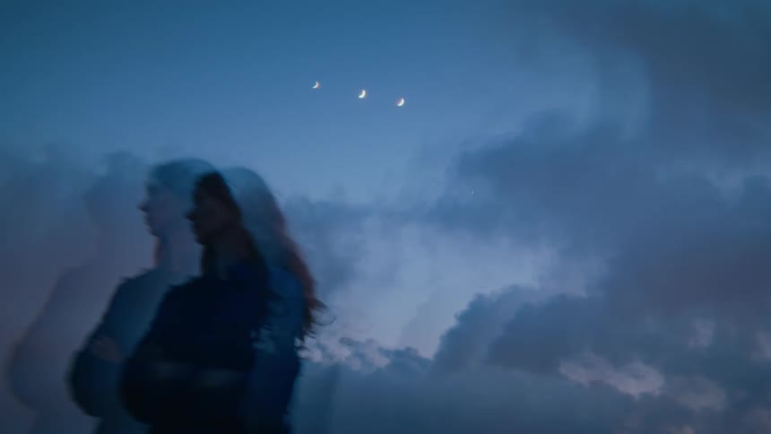 A surreal double exposure shows a womans ghostly image against a cloudy night sky with three crescent moons