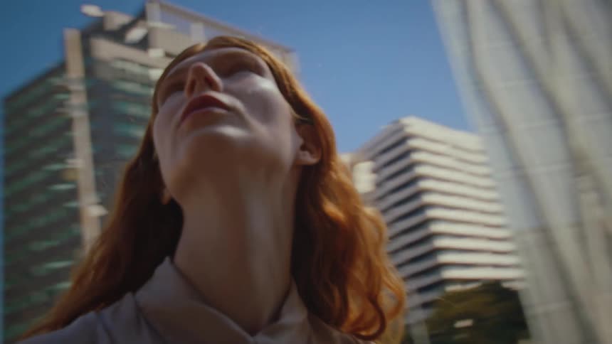 A young woman with red hair steps onto the city sidewalk observing the highrise buildings and skyscraper views at midday