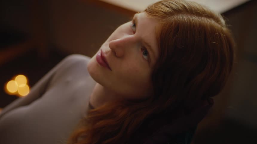 A woman with long red hair blinks her eyes then turns her head away