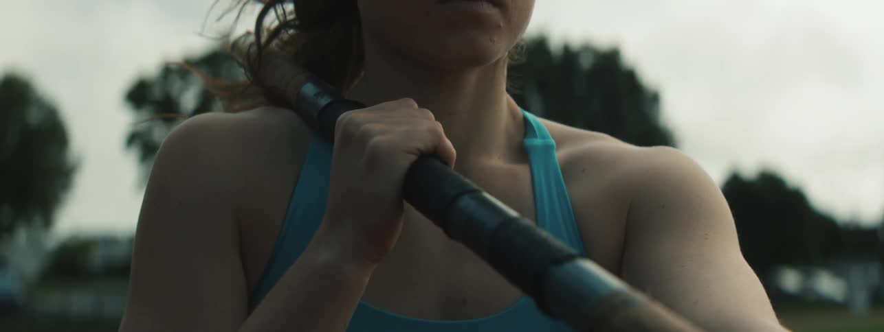 A focused young woman grips a rowing oar during an intense outdoor workout