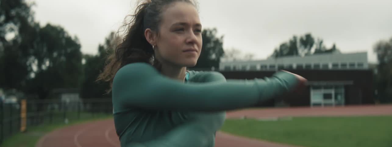 A teenage girl wearing sportswear stands on a track stretching and preparing for a race