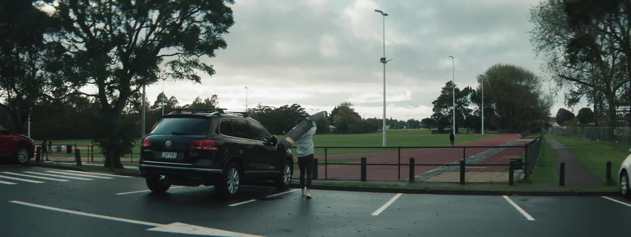 A woman carrying an item on top of a vehicle walks toward a track field on a cloudy day