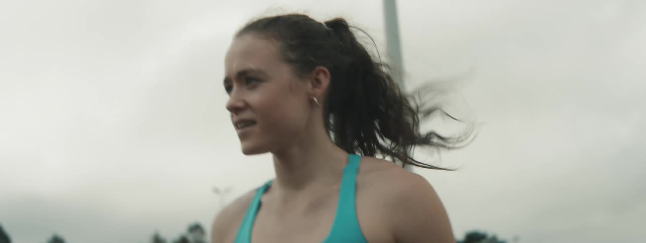 A young woman runs with a pole vault pole attempting a jump that fails on the track during a cloudy afternoon