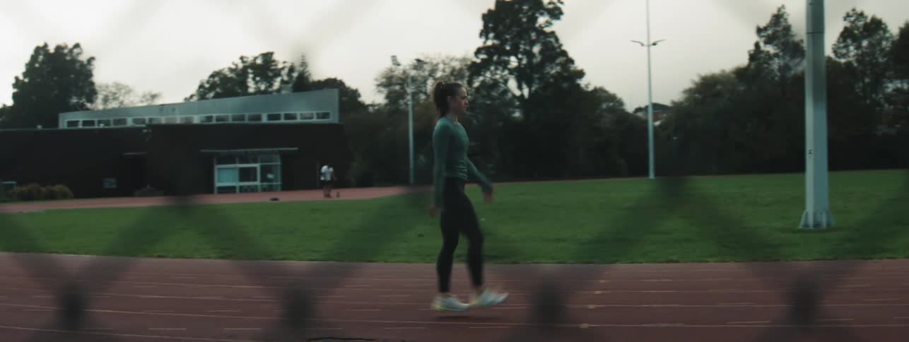 A woman is walking on a running track lifting her leg to stretch it
