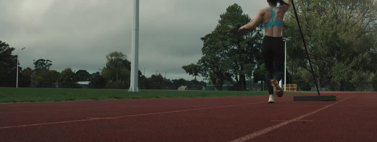 A pole vaulter runs down a track aiming at a wooden planting box to practice takeoff technique during training