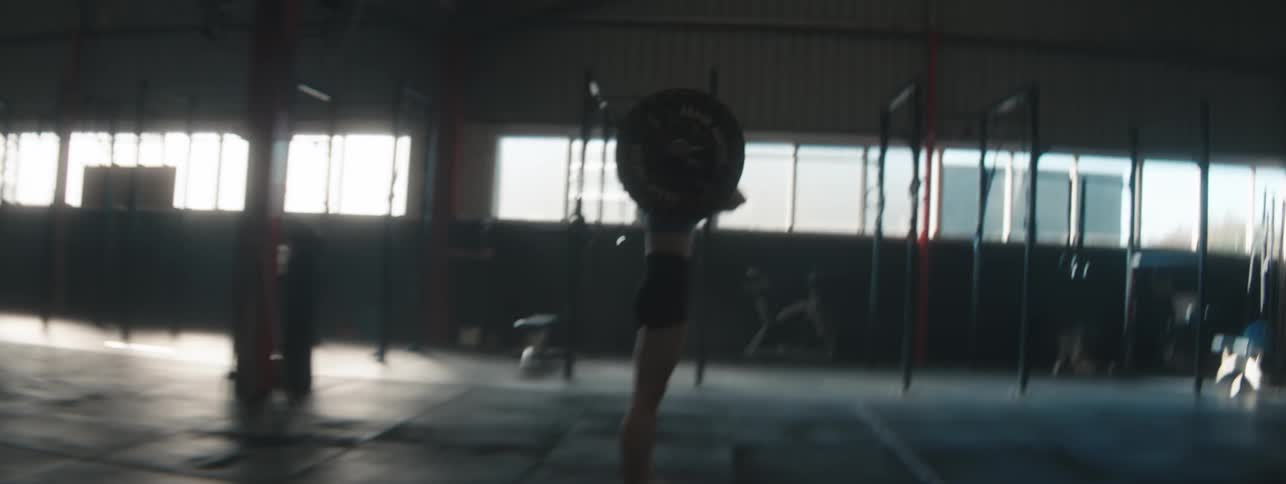 A woman lifts a heavy barbell inside a spacious gym