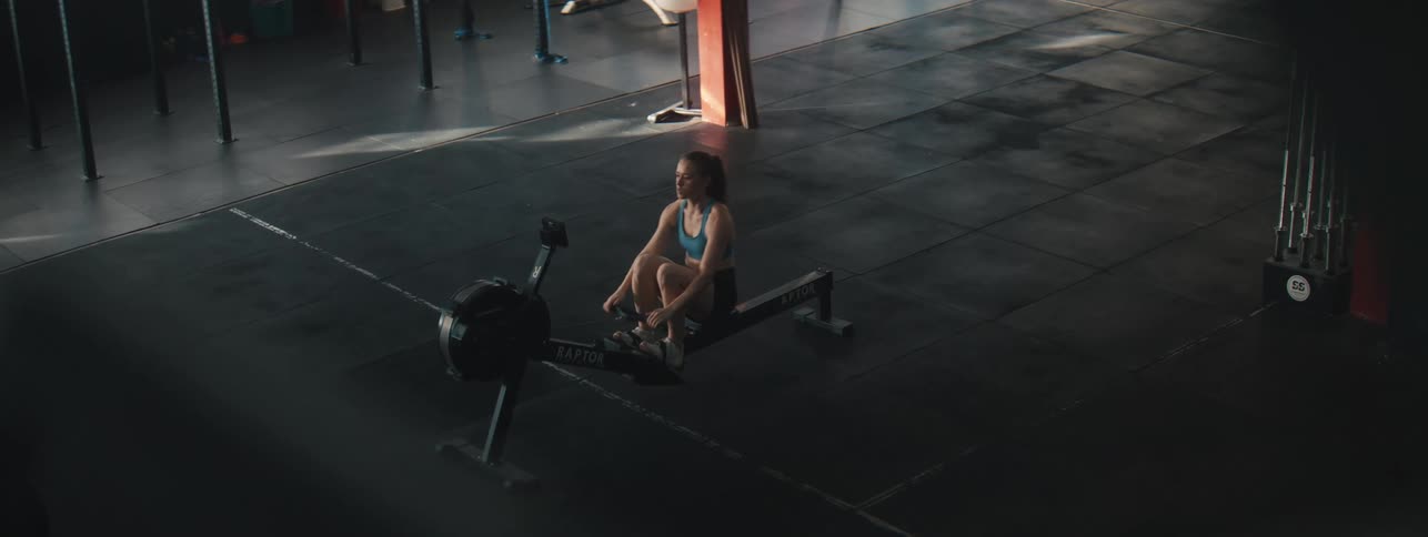 A woman is working out alone on a rowing machine in a mostly empty gym