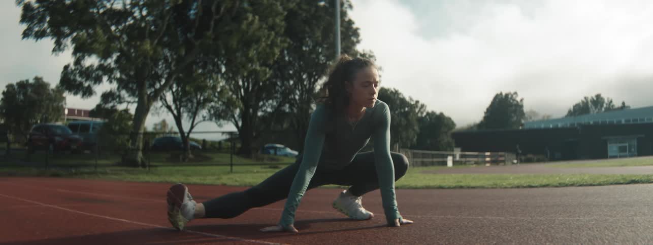 Young woman exercises by stretching outdoors on a racetrack in the middle of the day
