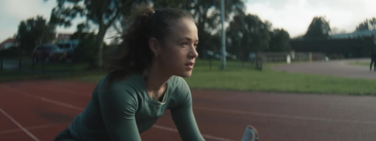 A female athlete is stretching on a running track during early morning light