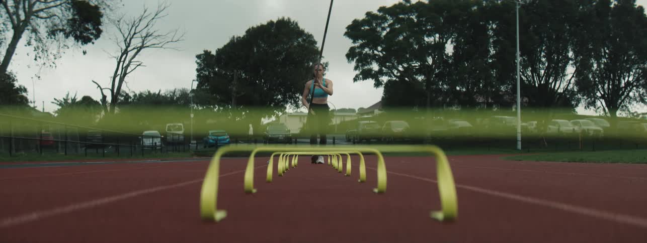 A pole vaulter sprints down the track holding a pole running through a series of yellow hurdles