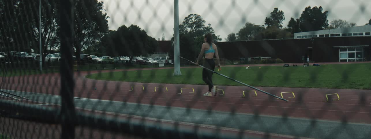 A woman runs on the track practicing a high jump with a pole