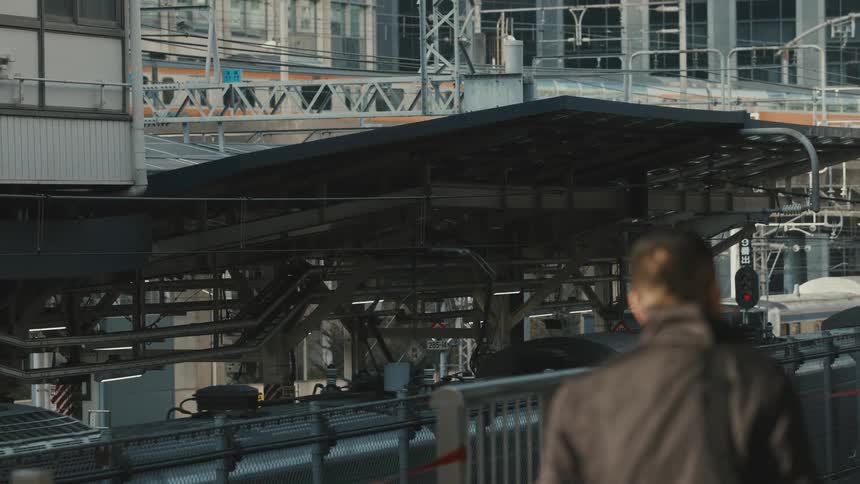 Pedestrians walk through the city while multiple electric trains pass nearby during the daytime