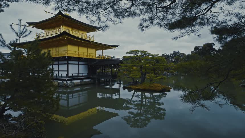 Yellow pagoda sits in the waters of a reflective lake surrounded by conifers on an overcast day
