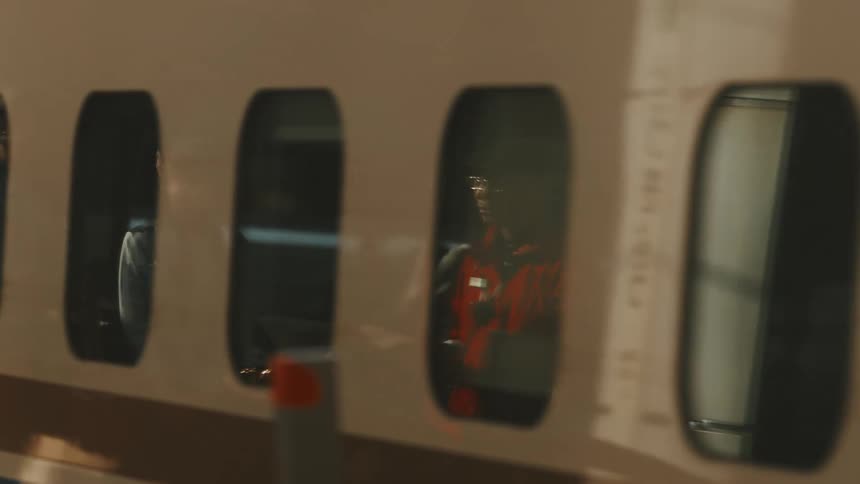 A train window reflects passengers waiting on the platform and a sign with japanese characters as the train departs