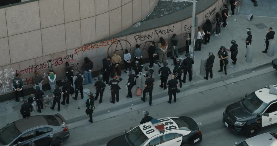 Police detain protesters lined up against a graffiticovered wall in an urban area