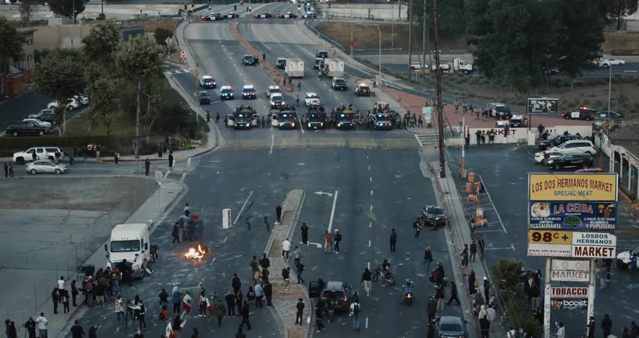 Protesters with fires and barricades gather on a city street facing a formidable police blockade of armored vehicles and officers on a highway overpass