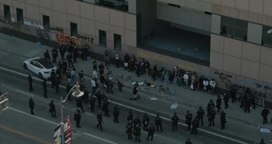 Aerial of a crowded city street with a group protesters surrounded by law enforcement personnel during daytime
