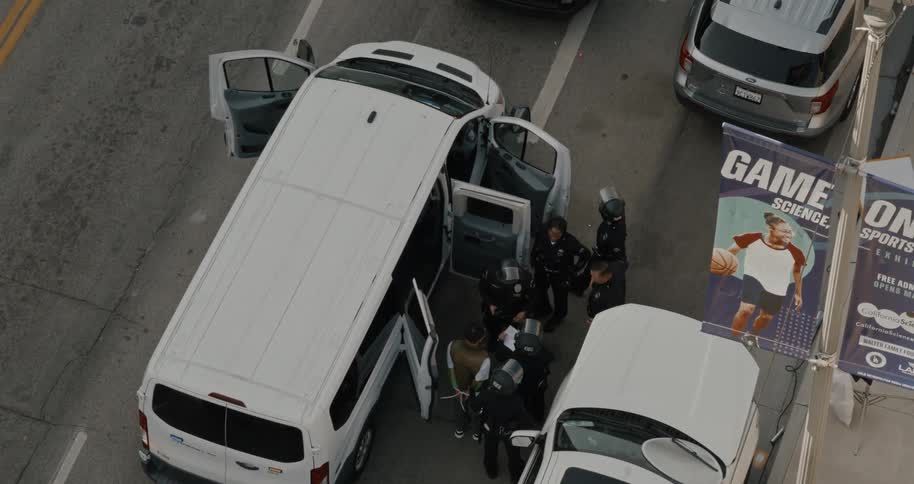 Police in tactical gear detain a person next to a white van during a street operation
