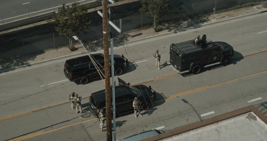 Heavily armed officers surround black suvs during a tactical operation on a city street