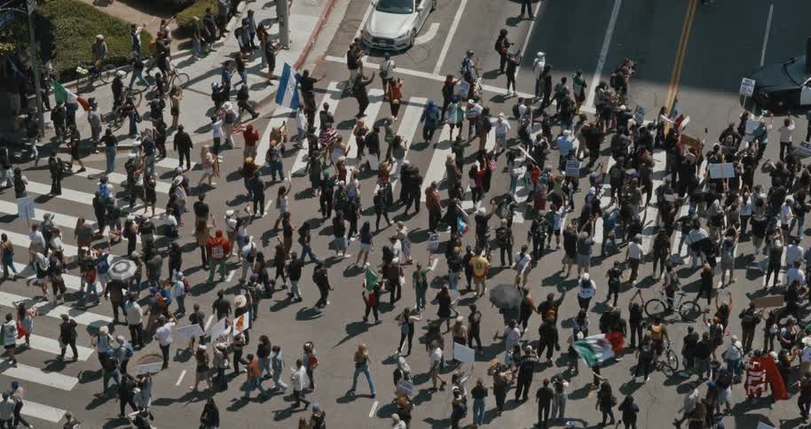 A large crowd gathers at a busy city intersection during a public protest or demonstration