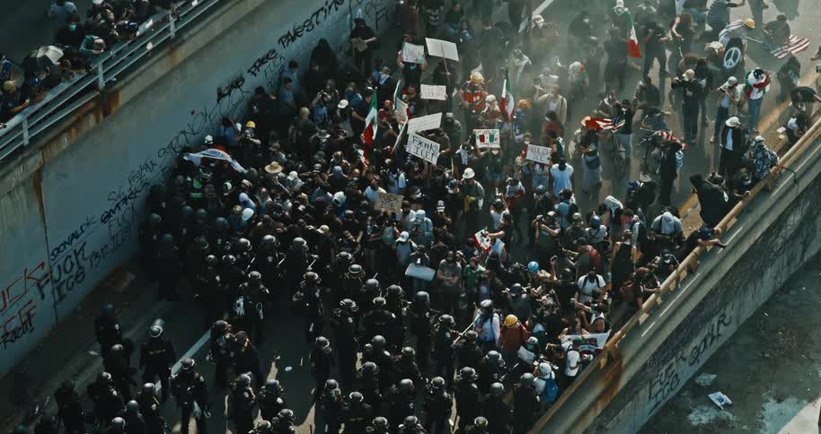A large crowd of protesters confronts a line of riot police on a graffiticovered underpass