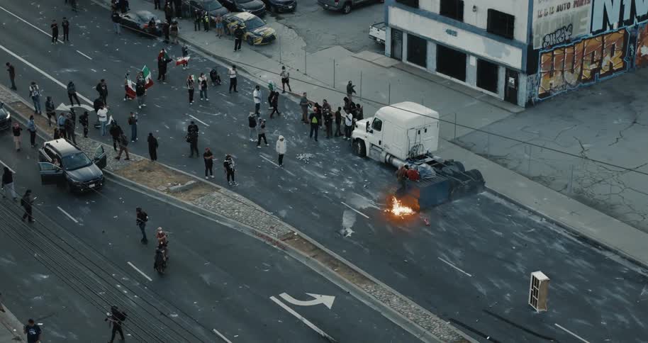 Protesters gather on a city street near a burning barricade and an abandoned truck