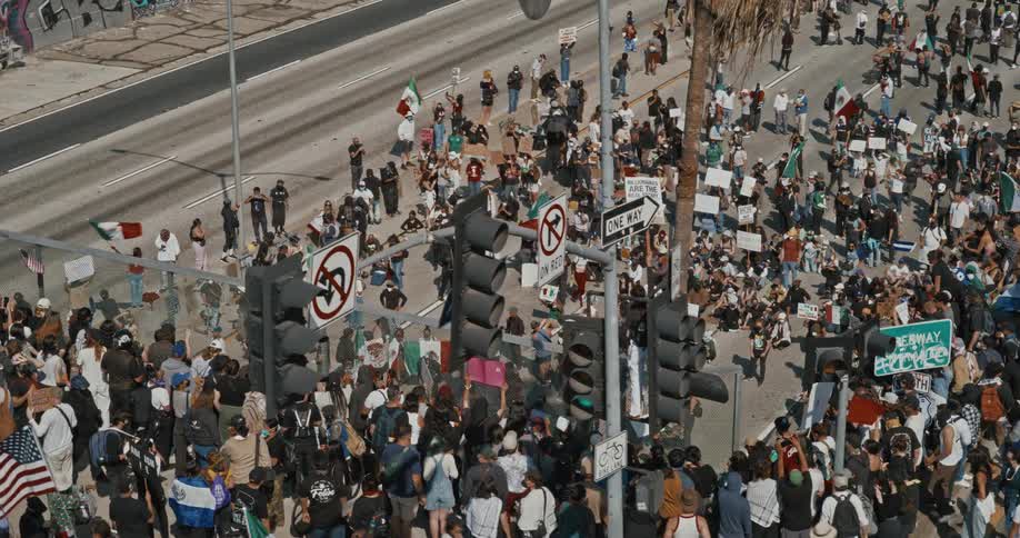 A large crowd gathers on a city street for a protest seen from above