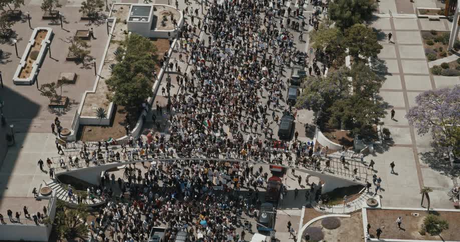 A large crowd fills a city street in a daytime protest seen from above