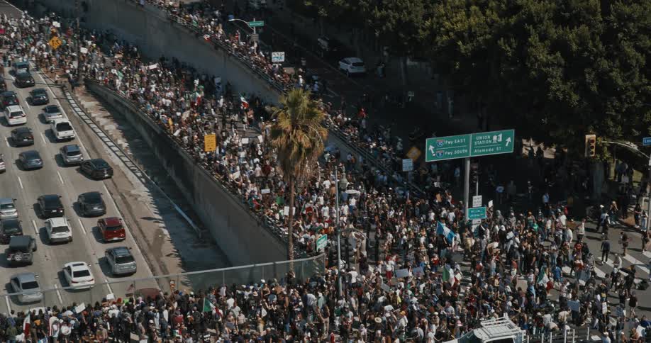 A protest involving a large crowd takes place in the city as people block sections of the road at midday