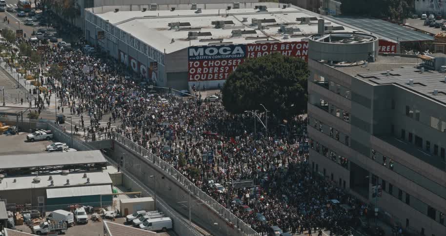 A large crowd of people is actively protesting in the streets in los angeles holding numerous signs and banners