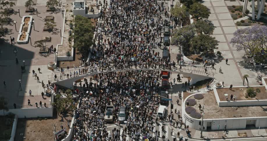 A large crowd of people is actively protesting in the streets of los angeles holding numerous signs and banners