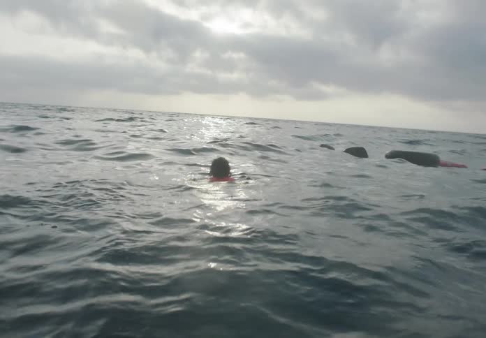 A young child wearing an orange life vest is bounced up and down by small waves in ocean