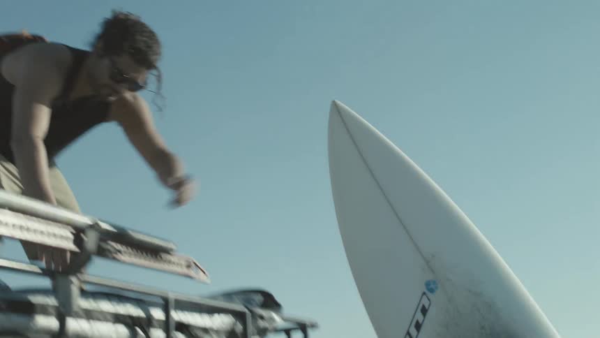 Man on top of jeep hands a surfboard down to another man on the ground