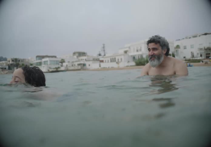 A man teaches his daughter how to swim in the ocean near the shore at midday