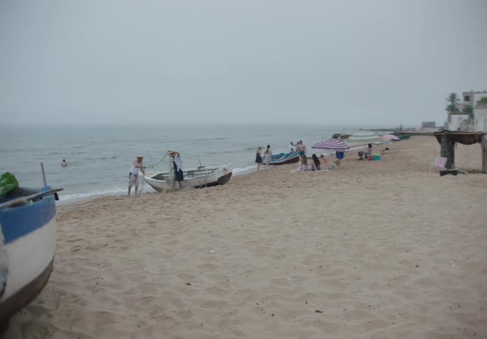 On an overcast day a group of children plays soccer on the beach while other beachgoers relax swim and work on small fishing boats