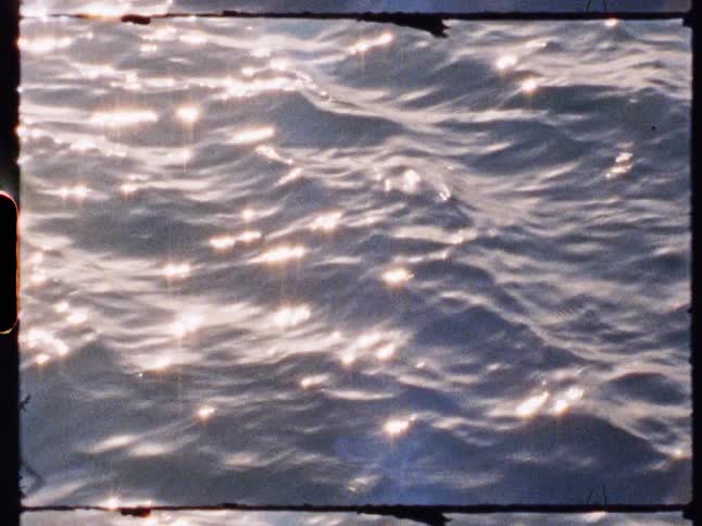 Sunlight sparkles and shimmers across the gentle ripples of the waters surface captured on grainy analog film with a visible frame border