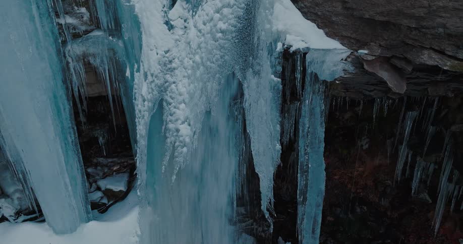 A wide icy blue waterfall cascades over rugged snowdusted rock formations