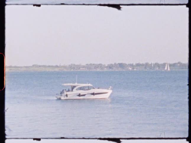 A white boat cruises across calm blue water near the shoreline