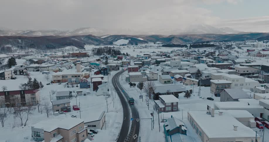 A snowy town with a winding road and houses is captured from above in winter
